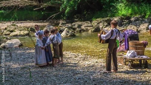 Kids are entertaining themselves while adults are washing clothes in the river. A young boy is also playing accordion. photo