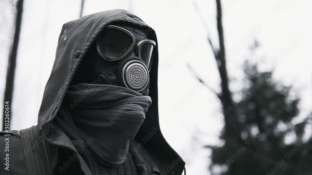Male wanderer in protective gas mask walking in empty dark forest. Stalker concept, portrait of lonely survivor after nuclear or chemical war. Post apocalyptic world. Stedicam following shot Male wanderer in protective gas mask walking in empty dark forest. Stalker concept, portrait of lonely survivor after nuclear or chemical war. Post apocalyptic world. Stedicam following shot