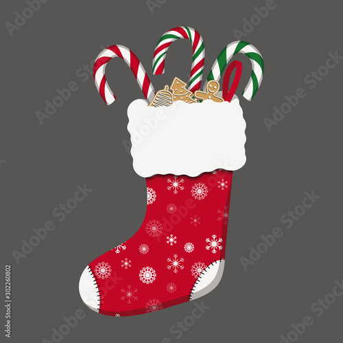 red Christmas stocking with candy canes and gingerbread on grey background