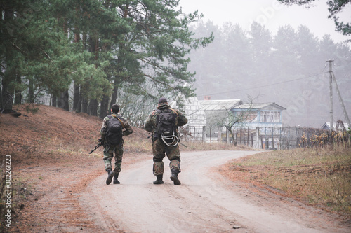 rear view, two soldiers with guns walk along a forest road © bisonov