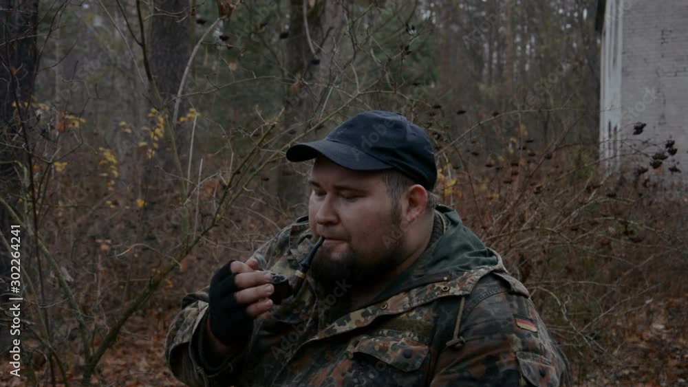 portrait of a man in camouflage who smokes a pipe against the background of a destroyed building hd stock footage portrait of a man in camouflage who smokes a pipe against the background of a destroyed building hd stock footage