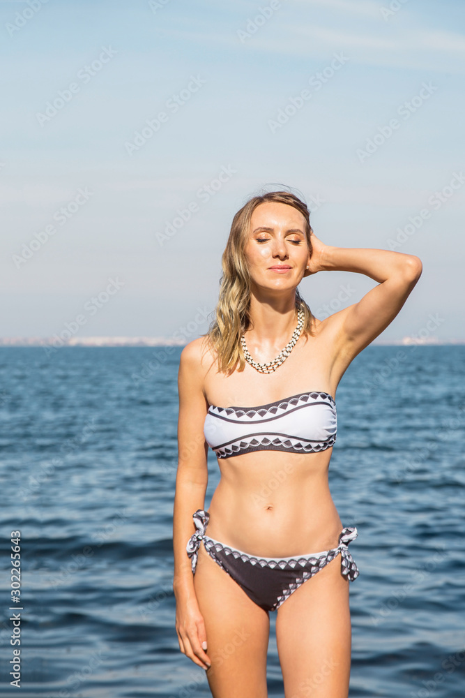 Slender Caucasian girl on the beach by the sea sunbathes in a swimsuit. Slender Caucasian girl on the beach by the sea sunbathes in a swimsuit.