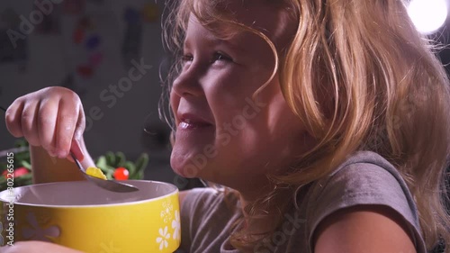 Cute little girl eating cornflakes from a yellow cup in the kitchen. Happy funny smiling baby face. Healthy babies food. Happy child eating. Children nutrition. Lunch or dinner, breakfast at home.