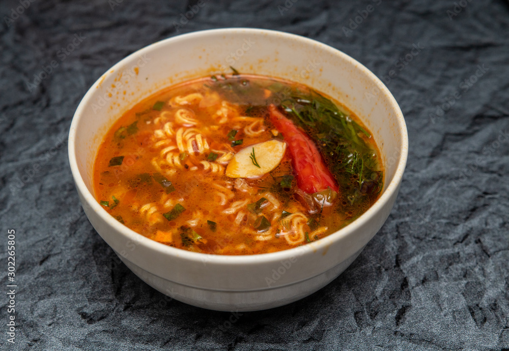 Noodle soup with tomatoes and herbs pepper in a plate on the table. Noodle soup with tomatoes and herbs pepper in a plate on the table.