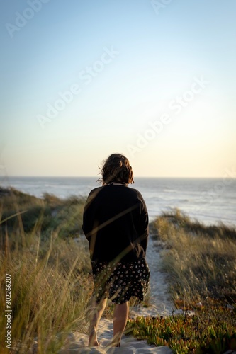 Woman view from behind standing on dune with sea in background in golden hour
