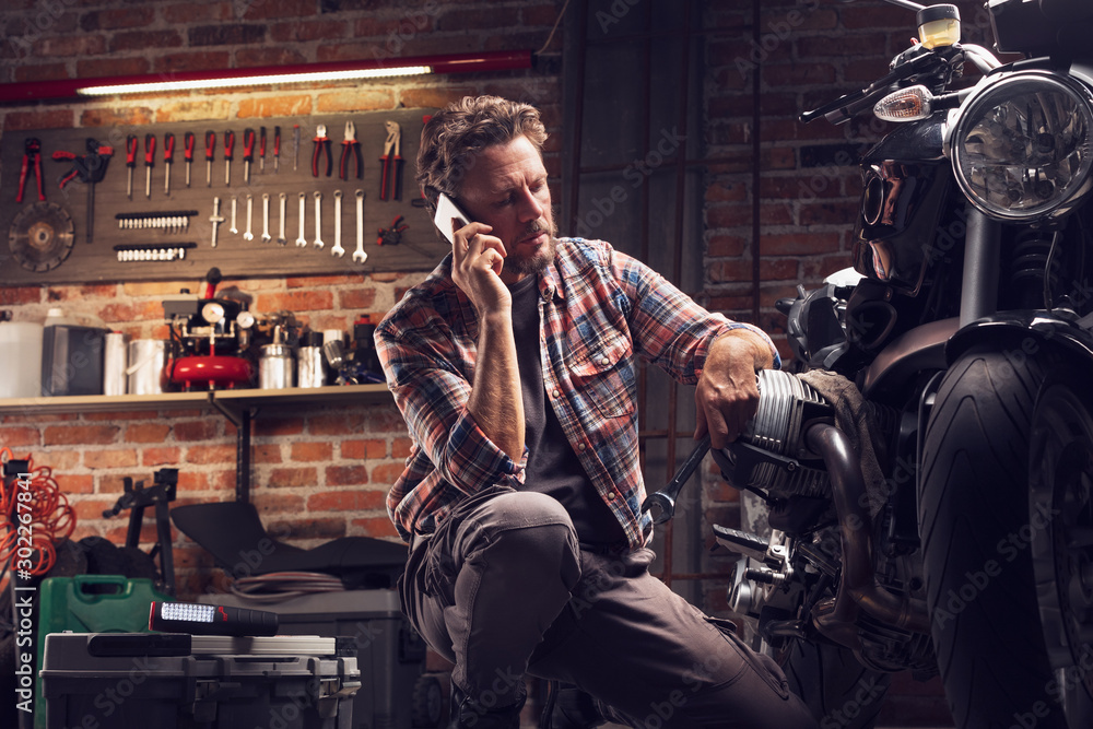 Man talking by the phone kneeling at motorcycle