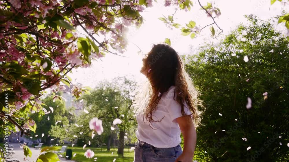 Millennial young girl have fun in flowering park. Cropped joyful woman dancing and moving under tree in petals falling from blossom cherry. Happy charming female enjoying sunny spring day at nature Millennial young girl have fun in flowering park. Cropped joyful woman dancing and moving under tree in petals falling from blossom cherry. Happy charming female enjoying sunny spring day at nature