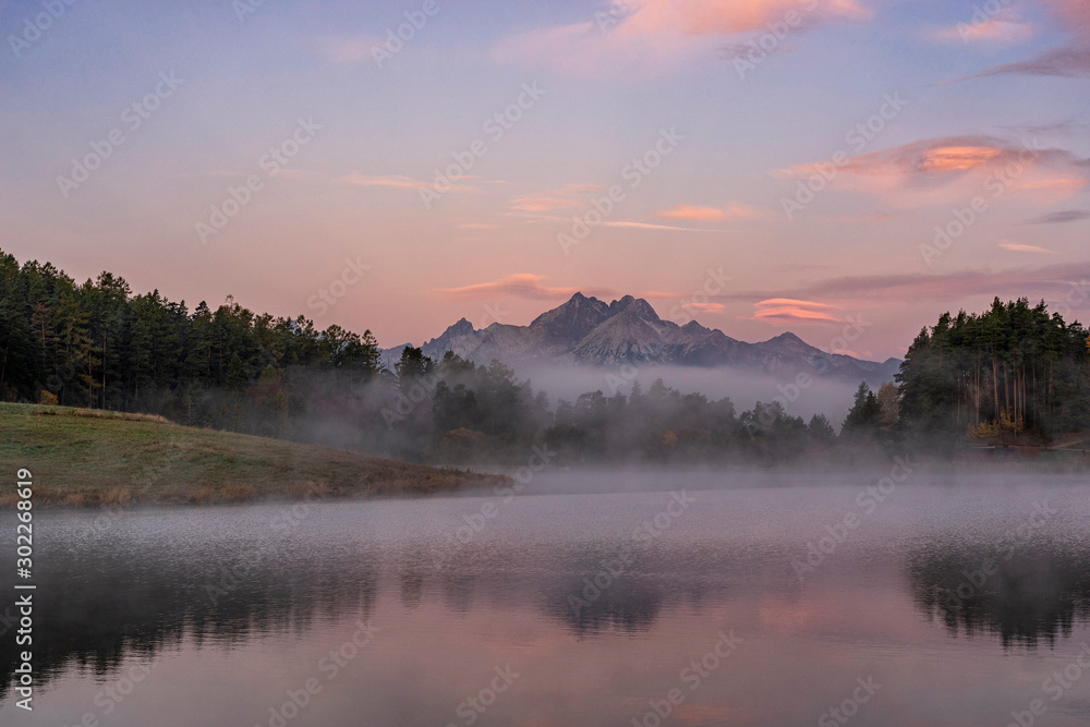Peaceful mountain scene with calm lake, colorful trees and high peaks in a golden warm light. Scenic view of High Tatras National Park, Slovakia.