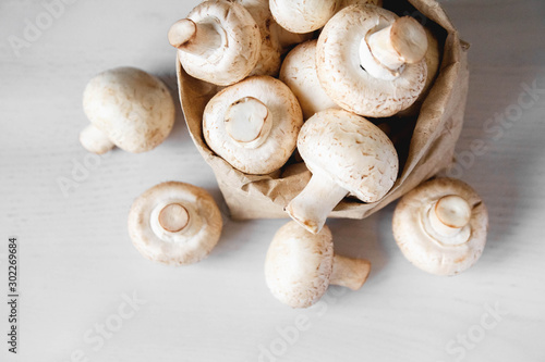 Mushrooms champignons in paper bag on a white wooden table. Place for text or advertising. Top view