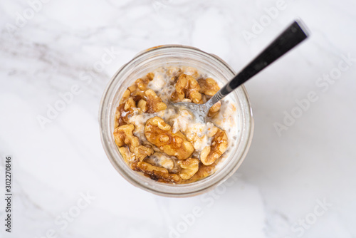 Overnight oats with chia seeds, walnuts and yogurt, on a white marble background.