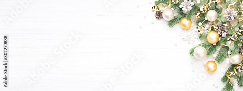Classic Christmas composition with fir branches, white and golden baubles, golden serpentine and pine cones on white wooden background. Noel banner for website.