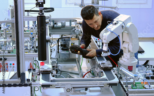 Man is programming robot arm with control panel which is integrated on smart factory production line. industry 4.0 automation line which is equipped with sensors and robotic arm. Selective Focus.