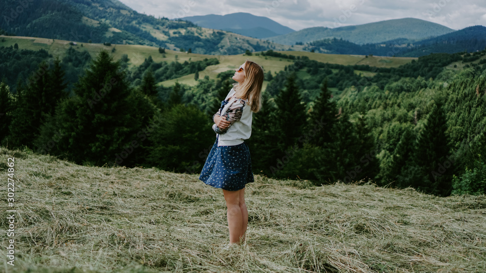 Naklejka premium Happy Woman standing on the mountain top looking at panoramic view of mountain range under blue sky