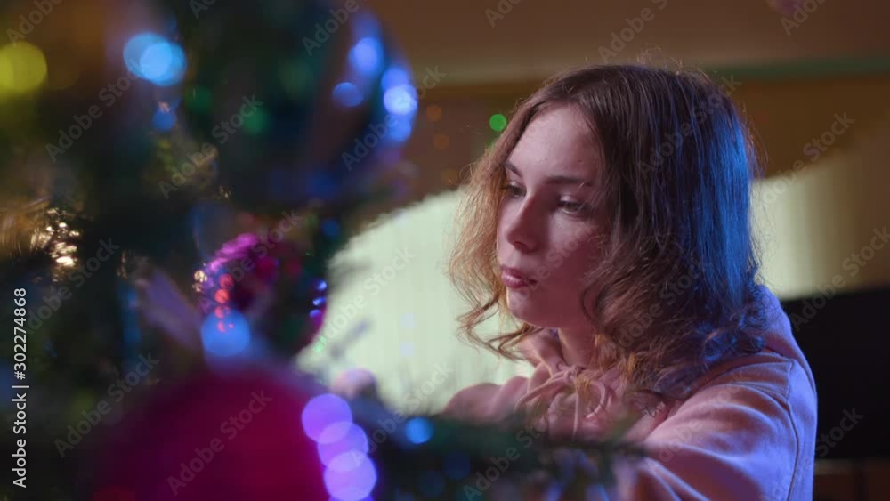 A nice young woman in a pink sweater loves decorating artificial Christmas tree branches. A nice young woman in a pink sweater loves decorating artificial Christmas tree branches.