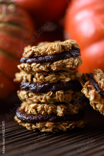 Healthy vegan dessert. Pile of homemade pumpkin oatmeal breakfast cookie sandwiches with dark chocolate and winter squashes on oak board