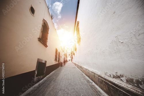 Fényképezés Beautiful shot of an alleyway in the middle of buildings with the sun shining in