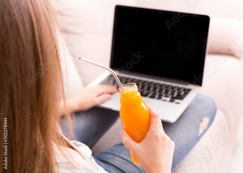 Woman working on laptop with black blank screen and drinking detox cocktail