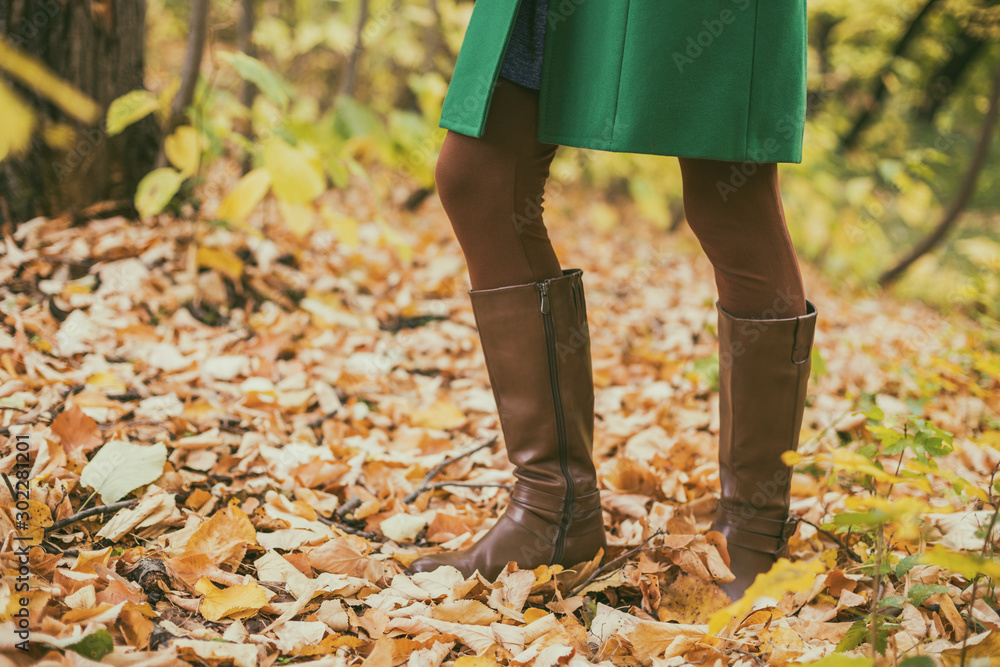 Close up photo of woman in boots surrounded with fall leafs while spending time in the park. Close up photo of woman in boots surrounded with fall leafs while spending time in the park.