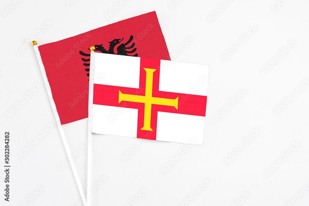 Guernsey and Albania stick flags on white background. High quality fabric, miniature national flag. Peaceful global concept.White floor for copy space.