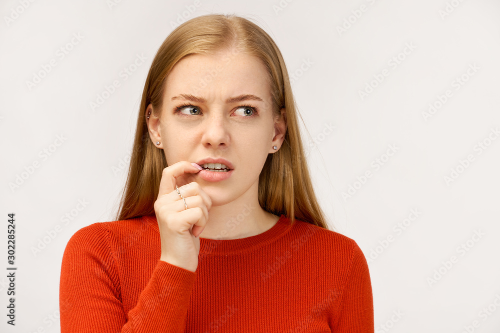 Fearful girl with frightened expression as notices large insect, trembles from fear, keeps hands near mouth. Beautiful girl with ginger long hair wearing red sweater, isolated on white wall in Studio. Fearful girl with frightened expression as notices large insect, trembles from fear, keeps hands near mouth. Beautiful girl with ginger long hair wearing red sweater, isolated on white wall in Studio.