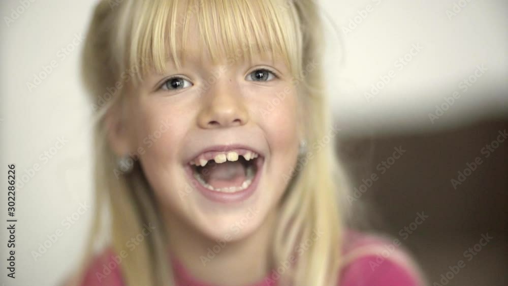 Face close-up portrait. blonde, beautiful little girl looking at the camera and laughing. no teeth Face close-up portrait. blonde, beautiful little girl looking at the camera and laughing. no teeth