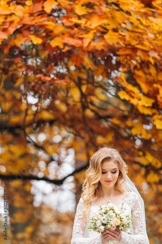 bride holds and looks at wedding bouquet on the background of tr