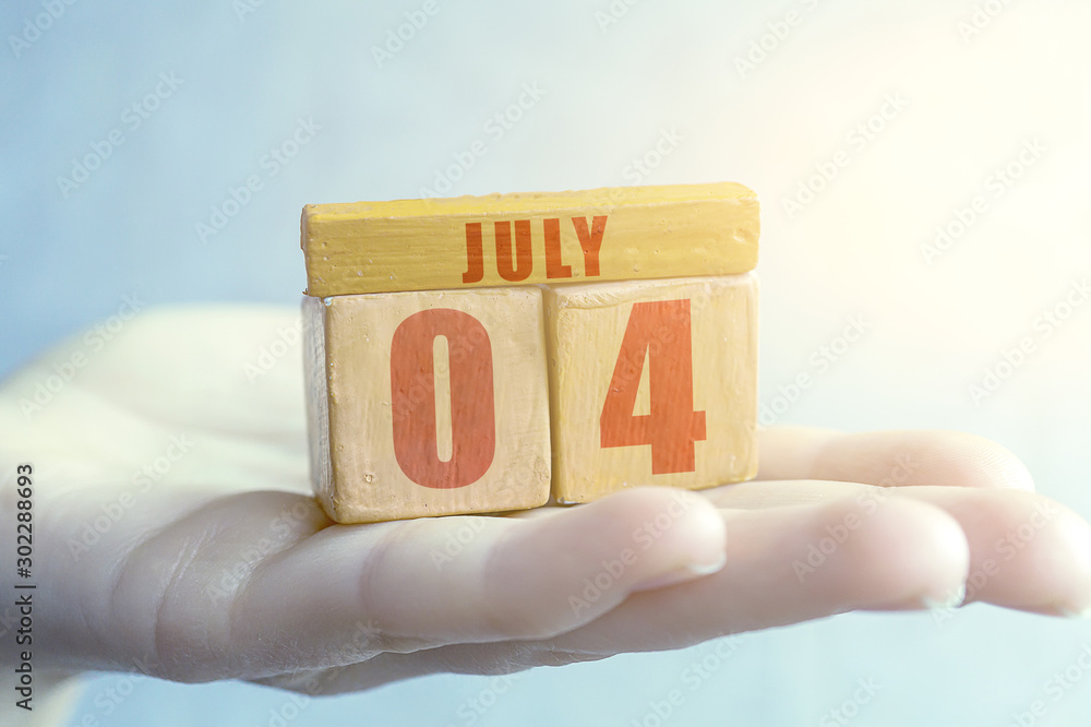 july 4th. Day 4 of month,Handmade wood cube with date month and day on female palm summer month, day of the year concept july 4th. Day 4 of month,Handmade wood cube with date month and day on female palm summer month, day of the year concept