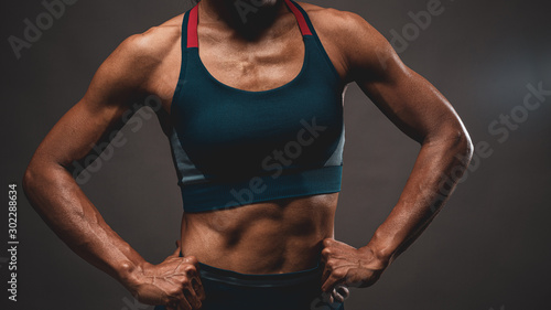 close up of the top part of muscle lean healthy body of 40 year old Asian woman in fitness training tops show the muscle and sweat after the training in the low light tone and dark background.