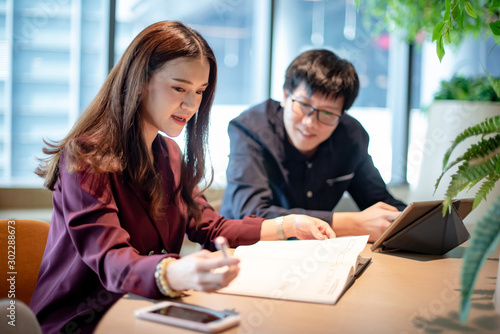 Business meeting and partnership concept. Attractive Asian colleagues talking about startup project report at workplace. Coworkers team having conversation sharing ideas together in conference room.