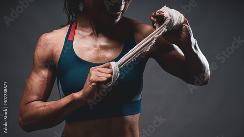 Close up of athletic healthy lean tone top body of asian woman holding white strap with both hands preparing for training or boxing while looking sideway with dark background.
