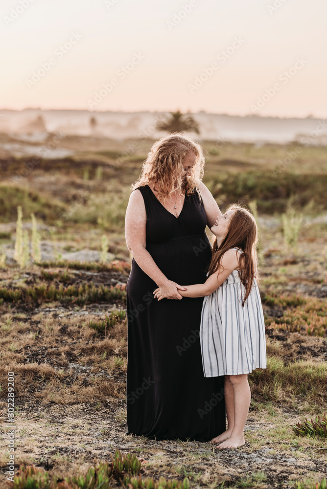 Portrait of redhead mother hugging young daughter at sunset at beach Portrait of redhead mother hugging young daughter at sunset at beach