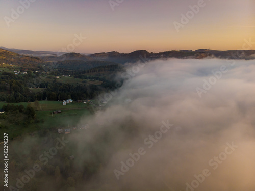 Fototapeta Naklejka Na Ścianę i Meble -  Beautiful morning panorama of forest fnd village covered by low clouds. Summer fog on the mountain hills. Misty woodland.