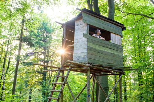 Woman in hunting stand, looking out at forest.