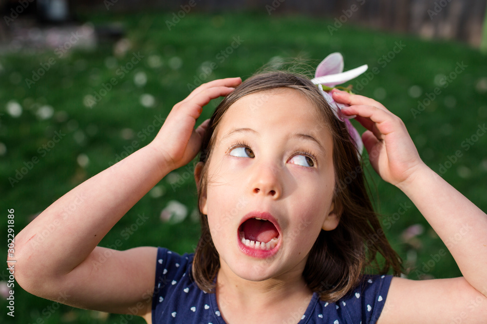 A small girl on a breezy day holds a flower blossom on head as a hat A small girl on a breezy day holds a flower blossom on head as a hat