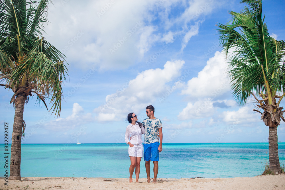 Young couple walking on tropical beach with white sand and turquoise ocean water in Caribbean