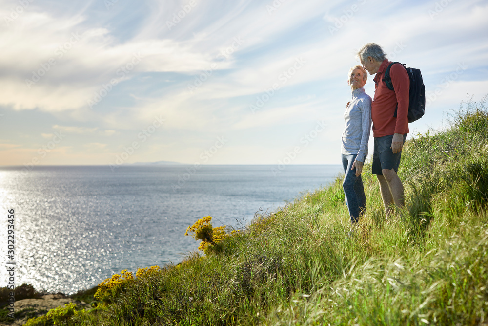 Senior couple talking while standing on cliff by sea against sky Senior couple talking while standing on cliff by sea against sky
