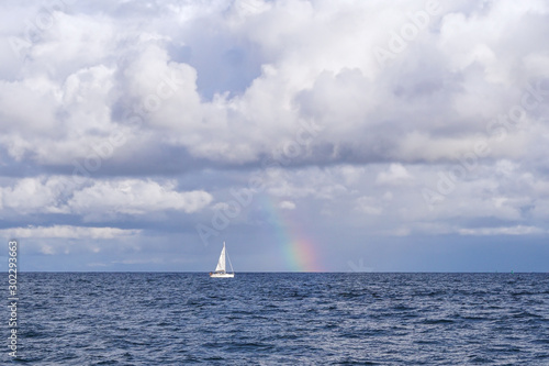 A small sailboat on the Baltic sea with a rainbow in the background