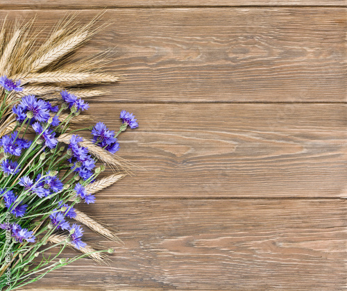 Blue cornflowers with wheat ears on a wooden background. Copy space.