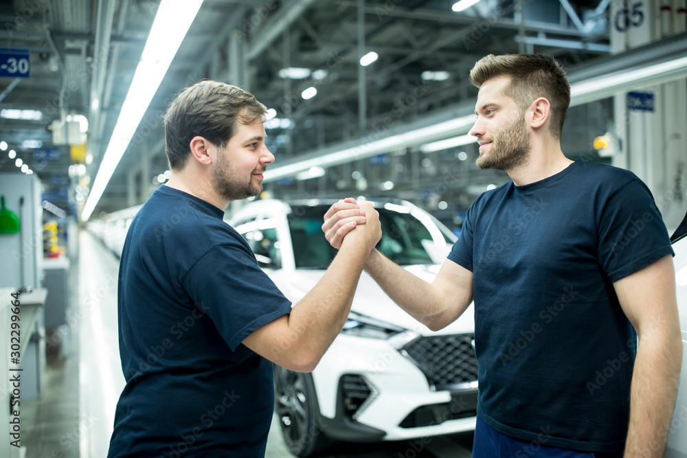 Two colleagues shaking hands in modern car factory Two colleagues shaking hands in modern car factory