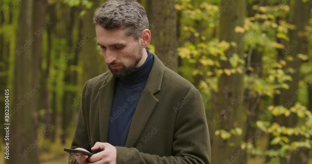 Portrait of a handsome gray-haired Caucasian man in the forest with the smartphone, shaking his head and taking picture of surroundings. Cinema 4k footage ProRes HQ. Portrait of a handsome gray-haired Caucasian man in the forest with the smartphone, shaking his head and taking picture of surroundings. Cinema 4k footage ProRes HQ.