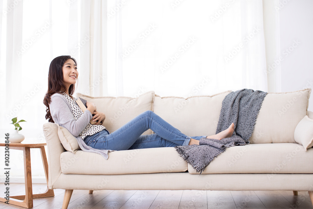 Happy young Chinese woman reading book on sofa Happy young Chinese woman reading book on sofa
