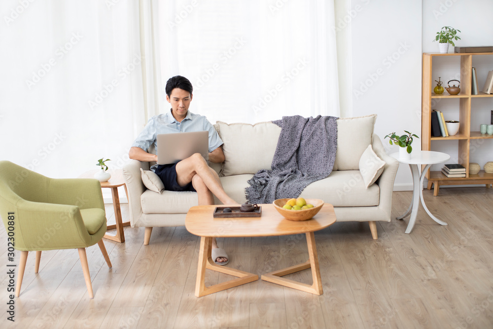 Young Chinese man using laptop in living room Young Chinese man using laptop in living room