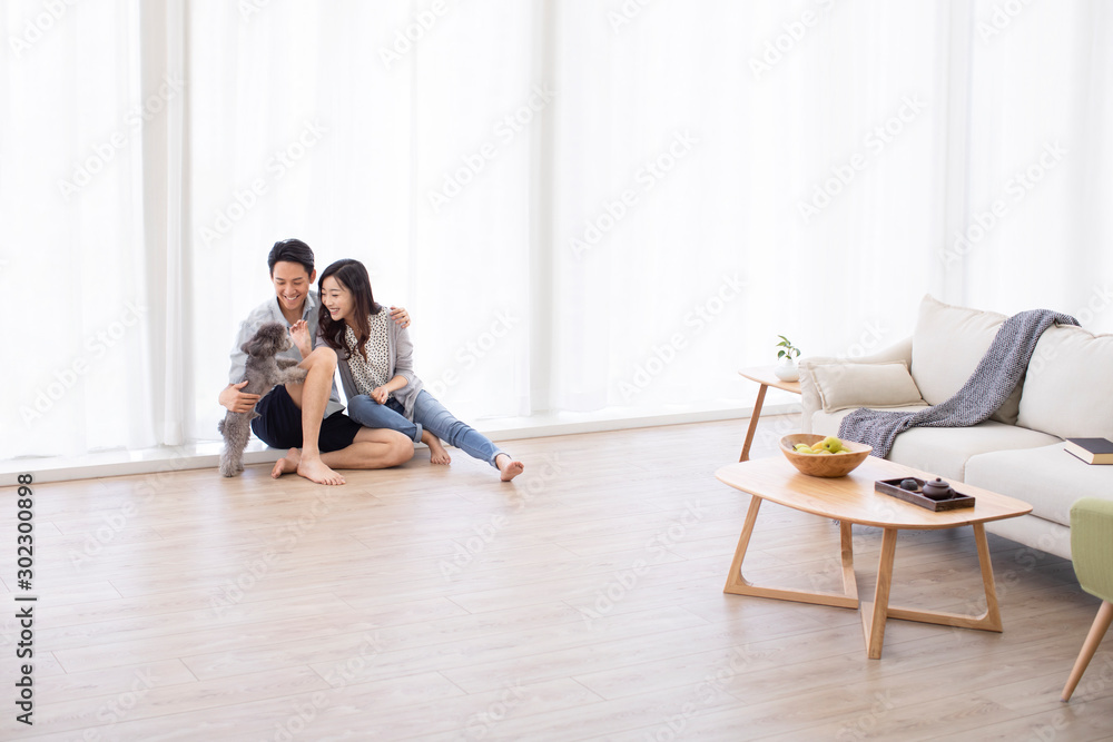 Happy young Chinese couple playing with dog in living room Happy young Chinese couple playing with dog in living room