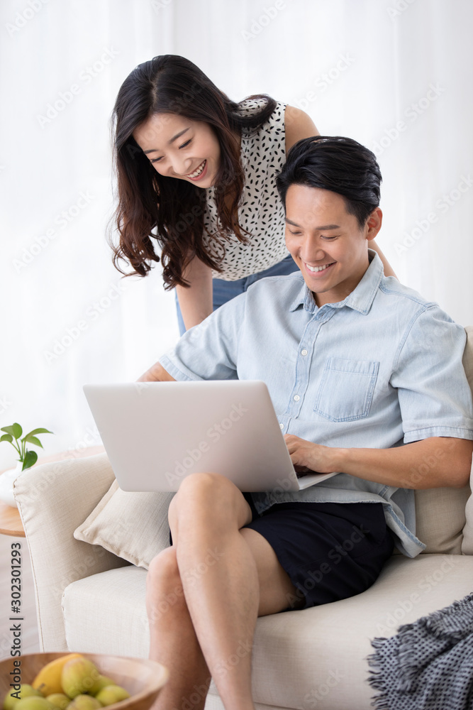 Happy young Chinese couple using laptop in living room