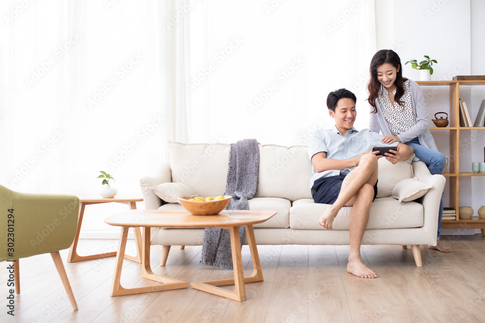 Happy young Chinese couple using smartphone in living room Happy young Chinese couple using smartphone in living room