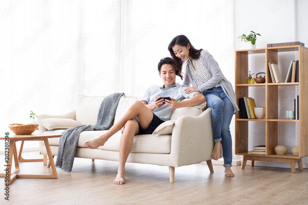 Happy young Chinese couple using smartphone in living room Happy young Chinese couple using smartphone in living room