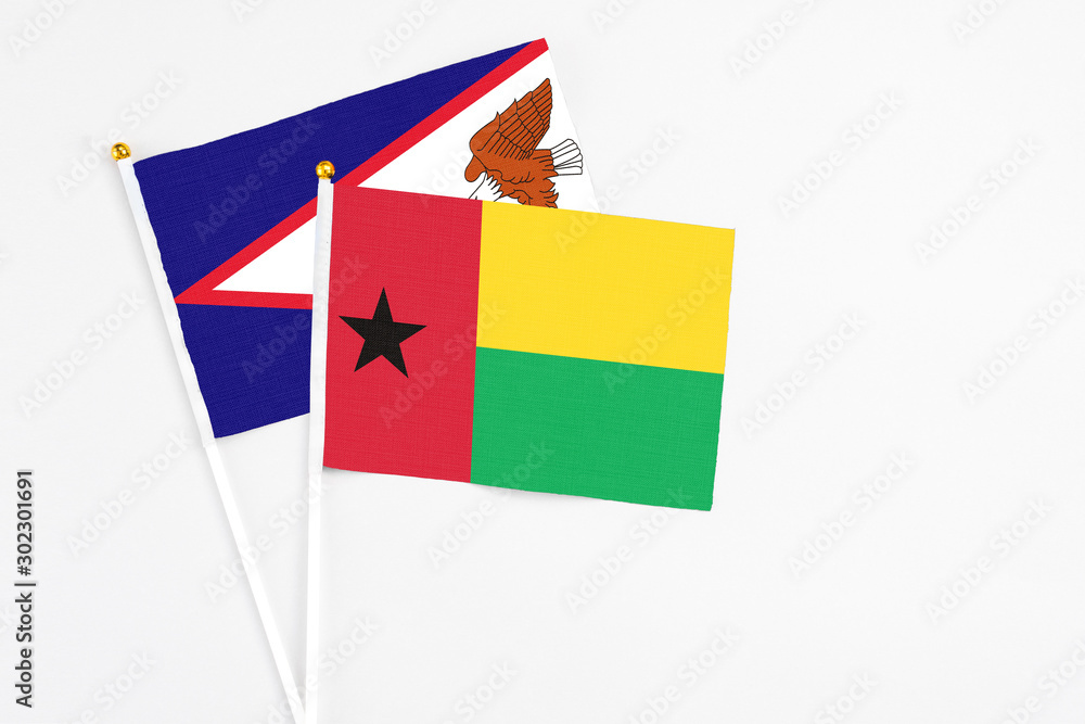 Guinea Bissau and American Samoa stick flags on white background. High quality fabric, miniature national flag. Peaceful global concept.White floor for copy space.