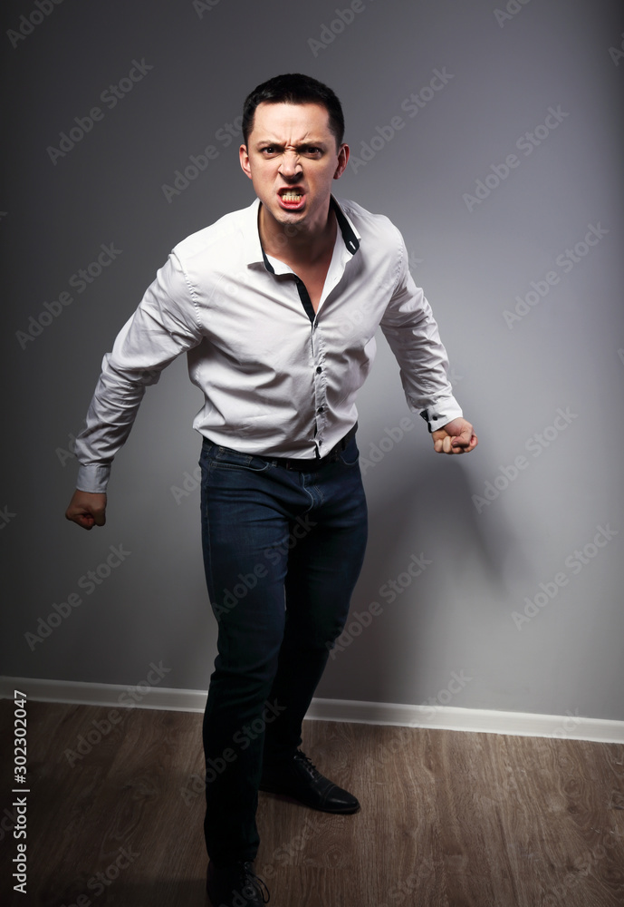 Angry young business man grimacing with aggressive eyes and holding hands with fiists on grey background. Closeup Angry young business man grimacing with aggressive eyes and holding hands with fiists on grey background. Closeup