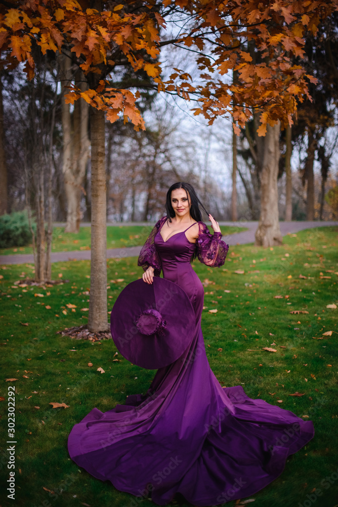 young woman in vintage silk dress is standing in autumn park