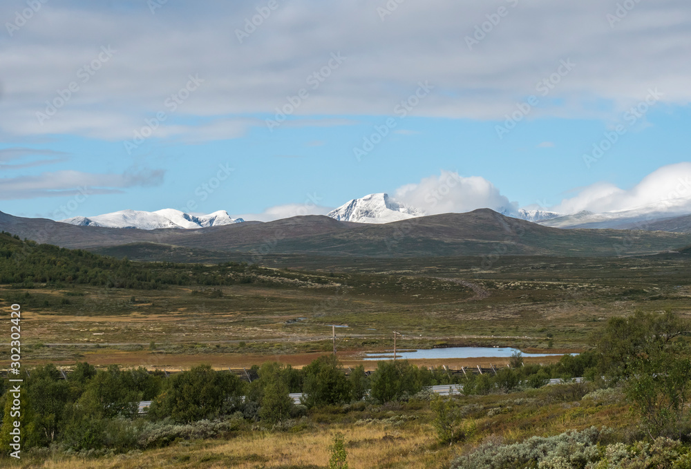 Autumn view on hills and snow capped mountains with dramatic clouds at Dovre Nasjonaalpark nature park from main road E6, Norway